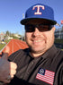 Man wearing a Texas Rangers cap and sunglasses, giving a thumbs-up on a track field.